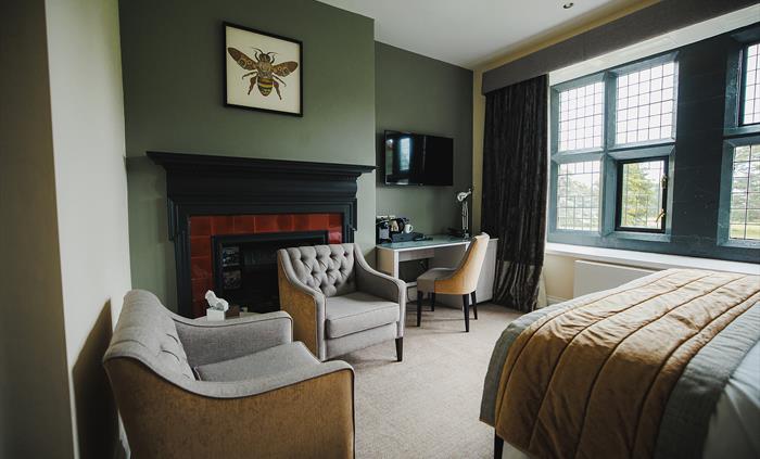 A hotel bedroom with arm chairs at foot of the bed and a tv on the wall.